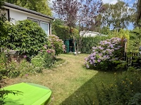 Blick in den Garten, umgeben von Hecken, mit Sandkasten für die Kinder
