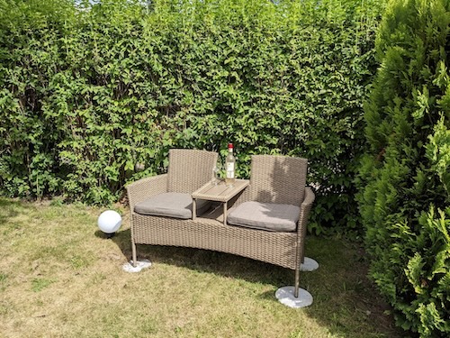 Gartenbank für 2 Personen mit integriertem kleinen Tisch und Weinflasche als Deko